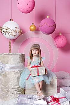 Pretty girl child 4 years old in a blue dress. Baby holding gift in their hands. Rose quartz room decorated holiday