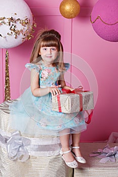 Pretty girl child 4 years old in a blue dress. Baby holding gift in their hands. Rose quartz room decorated holiday