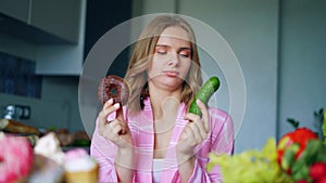 Pretty girl choosing between fresh cucumber or chocolate donut