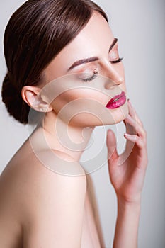 Pretty girl with closed eyes and dark hairs, with clean skin, with naked shoulders. A model with make-up and pink lips.