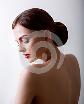 Pretty girl with closed eyes and dark hairs, with clean skin, with naked shoulders. A model with make-up and pink lips.