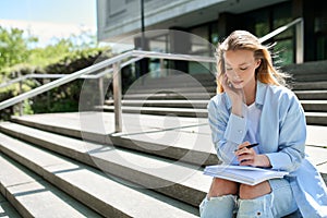 Pretty girl college student holding notebook sitting on stairs outside campus.
