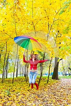 Pretty girl with colorful umbrella jumping in autumn park