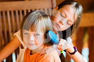 Pretty girl combing hair of younger sister