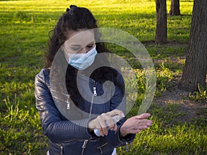 Pretty girl with curly hair in protective medical face mask disinfecting her hands with a sanitizer spray