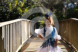 A pretty girl dancing flamenco in a typical gypsy dress with frills and fringes walks on a wooden bridge in a famous park in