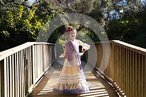 A pretty girl dancing flamenco in a typical gypsy dress with frills and fringes walks on a wooden bridge in a famous park in