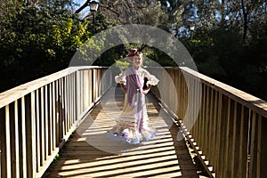 A pretty girl dancing flamenco in a typical gypsy dress with frills and fringes walks on a wooden bridge in a famous park in