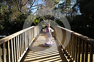 A pretty girl dancing flamenco in a typical gypsy dress with frills and fringes walks on a wooden bridge in a famous park in