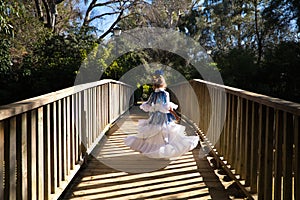 A pretty girl dancing flamenco in a typical gypsy dress with frills and fringes walks on a wooden bridge in a famous park in