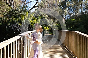 A pretty girl dancing flamenco in a typical gypsy dress with frills and fringes walks on a wooden bridge in a famous park in