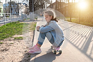 pretty girl in denim and pink sneakers sits on a penny board, a longboard . International Skateboarding Day.