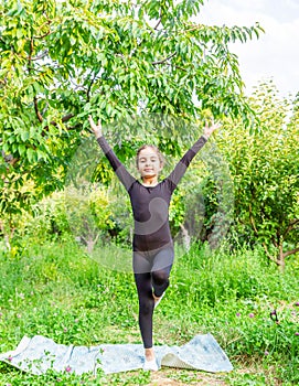 Pretty girl doing yoga exercises, little girl doing yoga exercises in the garden