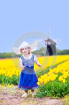 Pretty girl in Dutch costume in tulips field with windmill