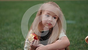 Pretty girl eating apple with classmates outdoors