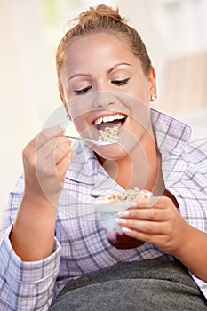 Pretty girl eating yoghurt at home dieting smiling