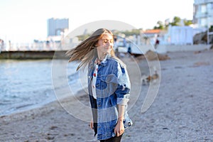 Pretty girl enjoying sea air, stands on seashore on sunny day.