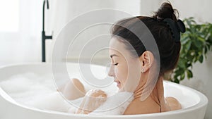 Pretty girl enjoying warm relaxing bath touching gentle white foam in bathroom