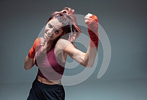 Pretty girl fighter in boxing bandages makes an uppercut in studio isolated on gray background. Strength and motivation