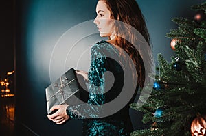 Pretty girl with gift box near Christmas tree, surprised