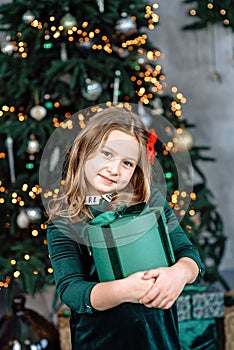 Pretty girl in green dress holding present gift box near decorated Christmas tree