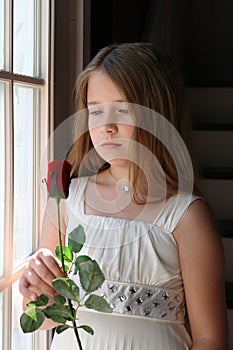 Pretty girl holding a red rose next to window