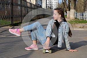 pretty girl in jeans and pink sneakers sits on a penny board and does exercises. International Skateboarding Day.