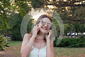 Pretty girl is listening to music in headphones outside. Favourite song. Woman is having rest in the park