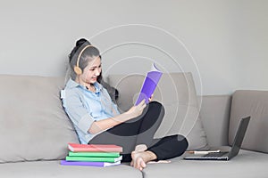 Pretty girl listening to music on headphones and reading on sofa in living room