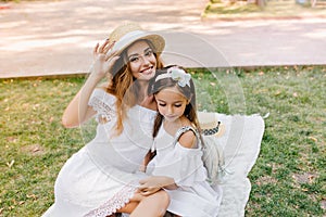 Pretty girl looking at lace on mother`s dress while she posing to camera on nature background. Gorgeous young woman with