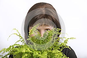 Pretty girl looks out from behind a flower. Young woman hid behind a potted indoor flower. Portrait of a florist