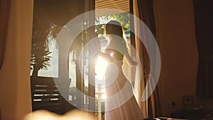 Brunette girl opens the door in the early morning during sunrise with lens flare effects