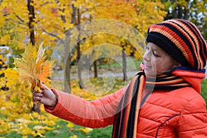 pretty girl in an orange jacket, beret and scarf holds bouquet of yellow maple leaves. Teenage girl walks in an autumn park