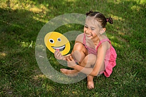 Pretty girl in pink polka dot dress laughing merrily and holding yellow emoticon