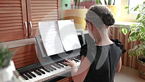 Pretty girl playing classic digital piano during family home concert, back view, smile at the end