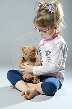 Pretty girl plays in the doctor treats a teddy bear on a gray ba