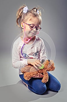 Pretty girl plays in the doctor treats a teddy bear on a gray ba