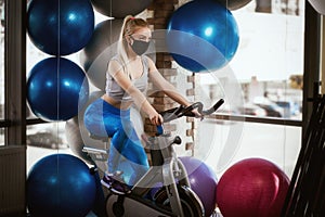 A pretty girl in a protective mask is engaged in an exercise bike. Protective masks against virus infection