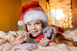 a pretty girl in a Santa hat writes a letter to Santa on the eve of Christmas, at home, lights and bokeh