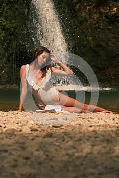 A pretty girl on the shore of a small mountain lake by a waterfall is fixing her wet hair