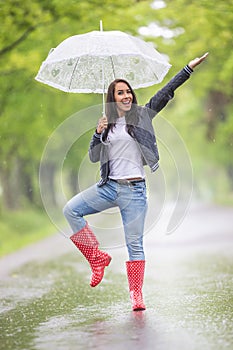 Pretty girl shows off in the rain holding a vintage umbrella, wearing red polka dot rain boots