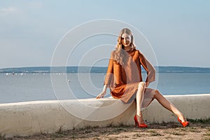 Pretty girl in silk dress sitting on pier with sea on background
