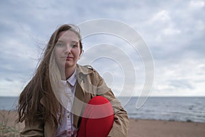 Pretty girl sitting on a beach in beige trench coat