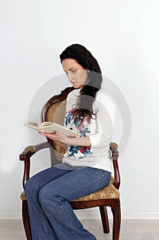 Pretty girl sitting in a chair and reading the book. studio