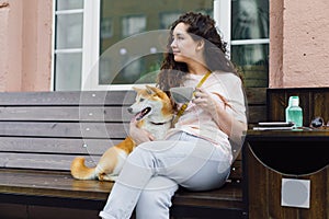 Pretty girl sitting in street cafe with cup of tea and shiba inu dog smiling