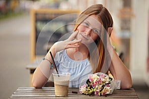 Pretty girl sitting at street cafe and drinking smoothies on urban background.