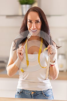 Pretty girl with slim waist holds fork in her hand with a meauring tape around her neck