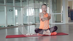 Pretty girl in sports clothes doing warm-up on the rug in the gym with tape