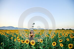 Pretty girl standing in background of sunflower field during sunset light.