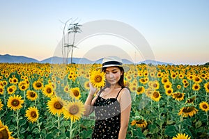 Pretty girl standing in background of sunflower field during sunset light.